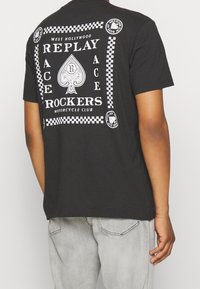 Czarny t-shirt z dużym białym wzorem graficznym z napisem i ikoną kielicha z tyłu. Krótkie rękawy, luźny fason, materiał bawełniany.