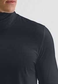 Schwarzes Rollkragenshirt aus glattem Stoff mit hohem Kragen. Mit einem dezenten geprägten Logo auf der Vorderseite. Eng anliegendes Design.