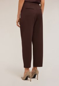 Pantaloni marroni a metà polpaccio con vita aderente, dotati di una tasca posteriore singola, abbinati a scarpe con tacco nude. Texture liscia.