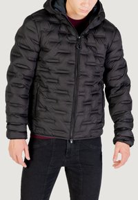 Giacca a vento nera con cappuccio, caratterizzata da un design trapuntato, chiusura con zip frontale e due tasche laterali. Tessuto liscio e materiale caldo.
