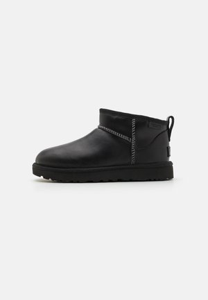Zwarte enkelboots van leer met een gladde afwerking, contrasterende stiksels, een ronde neus en een gestructureerde rubberen zool.