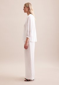 Top in lino bianco con maniche a sbuffo, abbinato a pantaloni larghi in lino bianco e sandali neri con tacco. Design semplice ed elegante.