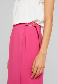 Fuchsia rok van een gladde stof, met een goudkleurige accentclip op de tailleband en zijplooien voor extra textuur.