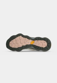 Semelle de chaussure avec bande de roulement extérieure noire et centre beige, présentant des motifs de grip profonds et un petit logo jaune au centre.