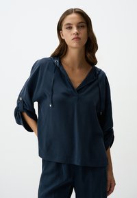 Maglione leggero blu navy con scollo a V, cordini regolabili e maniche arrotolate con dettagli in metallo argentato.