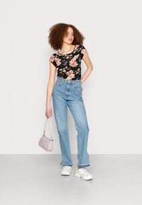 Top floral preto com mangas curtas, jeans de cintura alta azul claro, tênis brancos e uma pequena bolsa lilás clara.