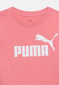 Ροζ μπλουζάκι με στρογγυλή λαιμόκοψη, με λευκή επιγραφή λογότυπου Puma και γραφικό ενός αλματώδους puma στο στήθος.