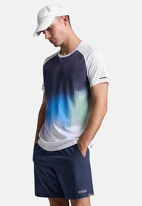 Ropa deportiva de rendimiento que consiste en una camiseta de manga corta en un degradado de azul a púrpura y pantalones cortos azul marino, complementada con una gorra blanca.