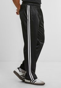 Black athletic pants with white side stripes, elastic waistband, and side pockets; made of smooth, lightweight fabric.