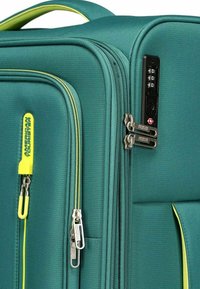 Maleta teal con acentos amarillos, tela texturizada, cremalleras dobles y cerradura TSA. Cuenta con un mango ergonómico y una etiqueta de marca adjunta.