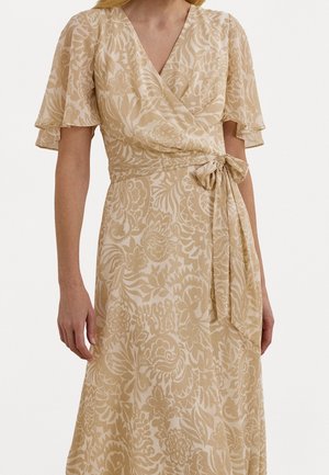 Frau trägt ein beiges Wickelkleid mit Blumenmuster, flatternden Ärmeln und einer an der Taille gebundenen Schleife.