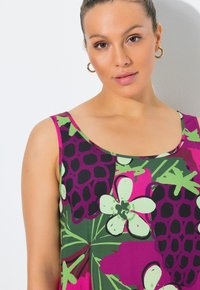 Blommig linne med ett livfullt mönster i lila, grönt och rosa med svarta detaljer. Gjord av mjukt tyg med rund halsringning.