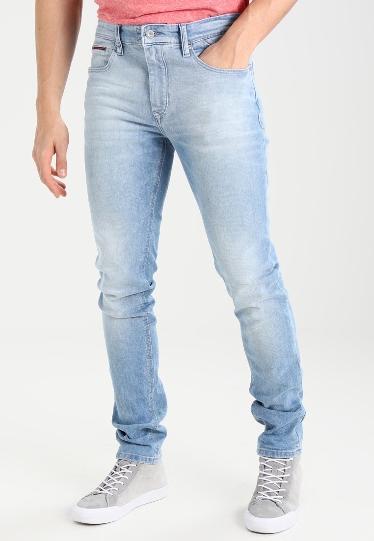 Ljust blå slim-fit jeans med subtila blekningar, fem fickor och en röd rand vid midjan, i kombination med grå hög-top sneakers.