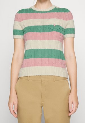 Femme portant un pull en maille à manches courtes avec des rayures horizontales roses, vertes et crème, associé à un pantalon beige.