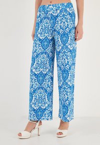Pantalone širokog kroja plave i bijele boje s cvjetnim i paisley uzorcima, izrađeni od glatkog materijala. U kombinaciji s bijelim sandalama na petu.