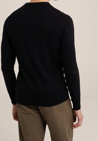 Svart stickad tröja med rund krage och långa ärmar, med en tight passform och ribbade muddarna. Matchad med khakibyxor.