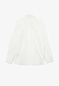 Camisa blanca de manga larga con cuello clásico, yugo trasero y puños abotonados. Textura suave y ajuste entallado.