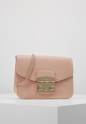Petit sac à main rose clair texturé avec une bandoulière en chaîne dorée et un fermoir rectangulaire doré sur une surface d'exposition blanche.