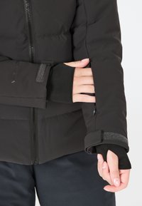 Doudoune noire avec fermeture éclair, poignets ajustables en Velcro et trous pour les pouces dans la couche intérieure pour un meilleur ajustement et une meilleure protection.