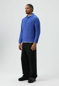 Blauwe fleece trui met kraag, lange mouwen en een getextureerde afwerking. Gecombineerd met zwarte wijde broekspijpen en stevige zwarte schoenen.