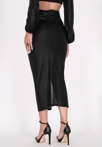 Gonna midi aderente nera realizzata in un tessuto strutturato, con zip sul retro e uno spacco laterale. Indossata con sandali neri con tacco alto.
