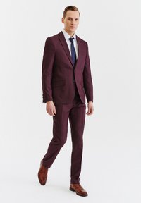 Bordowy garnitur w kratkę, dopasowany krój, wąskie klapy, dwie przednie kieszenie, zestawiony z białą koszulą i niebieskim krawatem w kropki. Brązowe skórzanebuty.