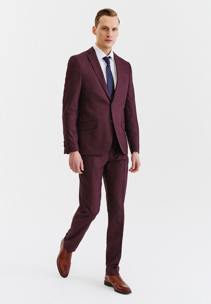 Bordowy garnitur w kratkę, dopasowany krój, wąskie klapy, dwie przednie kieszenie, zestawiony z białą koszulą i niebieskim krawatem w kropki. Brązowe skórzanebuty.