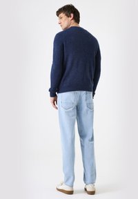Marineblauer Strickpullover mit Rundhalsausschnitt, kombiniert mit hellblauen, locker sitzenden Jeans. Der Pullover hat gerippte Bündchen und einen gerippten Saum.