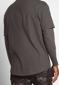 Dark gray short-sleeve t-shirt layered over a long-sleeve black top, featuring a relaxed fit and smooth cotton texture.