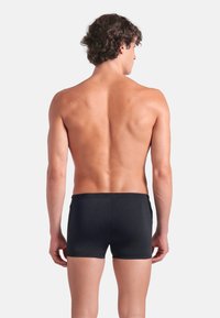 Svarta boxershorts i ett glansigt tyg, med en tight passform och elastisk midja, sedda bakifrån utan några ytterligare detaljer.