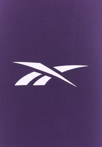 Lila tyg med en stor vit logotyp med skarpa, vinklade detaljer. Texturen ser jämn och konsekvent ut över ytan.