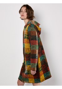 Kapturowana, wielokolorowa kurtka w kratę w ciepłych odcieniach czerwieni, zieleni i żółci; posiada pełny zamek błyskawiczny i boczne kieszenie. Miękki, teksturowany materiał.