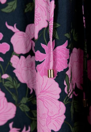 Roze bloemenstof met grote bloesems op een donkere achtergrond. Heeft een gouden metalen accent op een trekkoord. Zachte textuur en levendige kleuren.