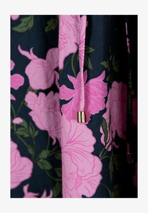 Roze bloemenstof met grote bloesems op een donkere achtergrond. Heeft een gouden metalen accent op een trekkoord. Zachte textuur en levendige kleuren.