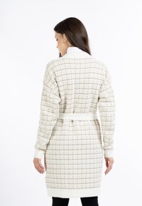 Cremefarbener gestrickter Cardigan mit einem strukturierten Muster, einem Gürtel in der Taille und gerippten Bündchen, der in mittellanger Ausführung gestaltet ist.