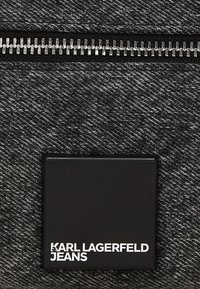 Fekete bőr folt fehér "KARL LAGERFELD JEANS" szöveggel sötétszürke farmeranyag alatt egy ezüst szippantóval.