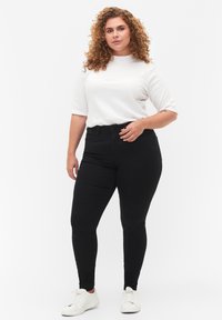 Black skinny jeans paired with a white ribbed shirt. The jeans have a smooth texture; the shirt features a high neckline and short sleeves.