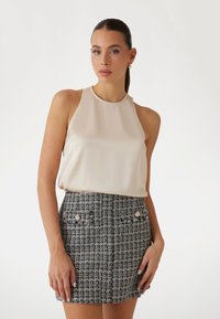 Top halter din satin crem, asociat cu o fustă mini din tweed alb-negru; fusta are două buzunare frontale cu butoane decorative.