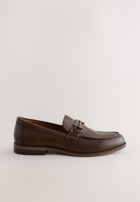 Mocassin homme en cuir marron avec détail de boucle métallique et petit talon, présenté de profil sur un fond clair uni.