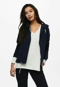 Navy blue lightweight jacket with a hood, zipper, drawstring hem, and two side pockets, layered over a white V-neck top.