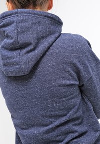 Sweat à capuche bleu marine en tissu texturé, avec une grande capuche et une coupe ample. Le dos présente des coutures prononcées et un matériau doux.