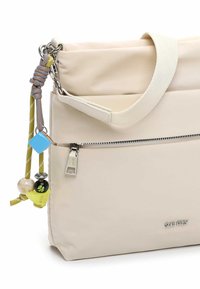 Beżowa syntetyczna torba z klapką na górze, zamkiem błyskawicznym i ozdobnymi zawieszkami na pasku. Charakteryzuje się gładką fakturą i eleganckim designem.