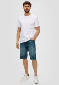 Biała bawełniana koszulka w zestawie z niebieskimi, zdartymi szortami dżinsowymi o luźnym kroju i długości do kolan. Uzupełniona białymi sneakersami.