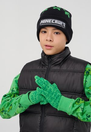 Gilet imbottito nero, maniche lunghe a tema Minecraft in verde pixelato, guanti verdi con design testurizzato e un berretto nero con il logo del marchio.