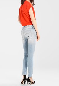 Skinny blue jeans with distressed detailing, paired with a red short-sleeve top and black heels featuring white polka dots.