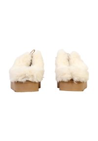 Chaussons en fausse fourrure avec une texture blanche douce, semelle plateforme en bois beige et petite boucle à l'arrière pour un enfilage facile. Forme arrondie sans logo visible.