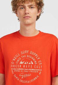 Camiseta de algodón naranja con un gráfico circular blanco que presenta texto y diseños de olas en la parte frontal. Mangas cortas y cuello redondo.