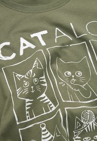 Olive green cotton t-shirt featuring white graphic prints of four cats in panels, displaying various facial expressions and designs.
