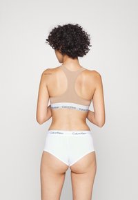 Sportivo top in un marrone chiaro con design racerback. Slip alti bianchi con banda logo Calvin Klein. Tessuto dalla superficie liscia.
