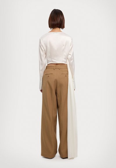 Κομμένη λευκή σατέν μπλούζα με μακριά μανίκια, συνδυασμένη με ψηλόμεσες καμηλό παντελόνες τύπου wide leg οι οποίες διαθέτουν πίσω τσέπες και κουμπιά.